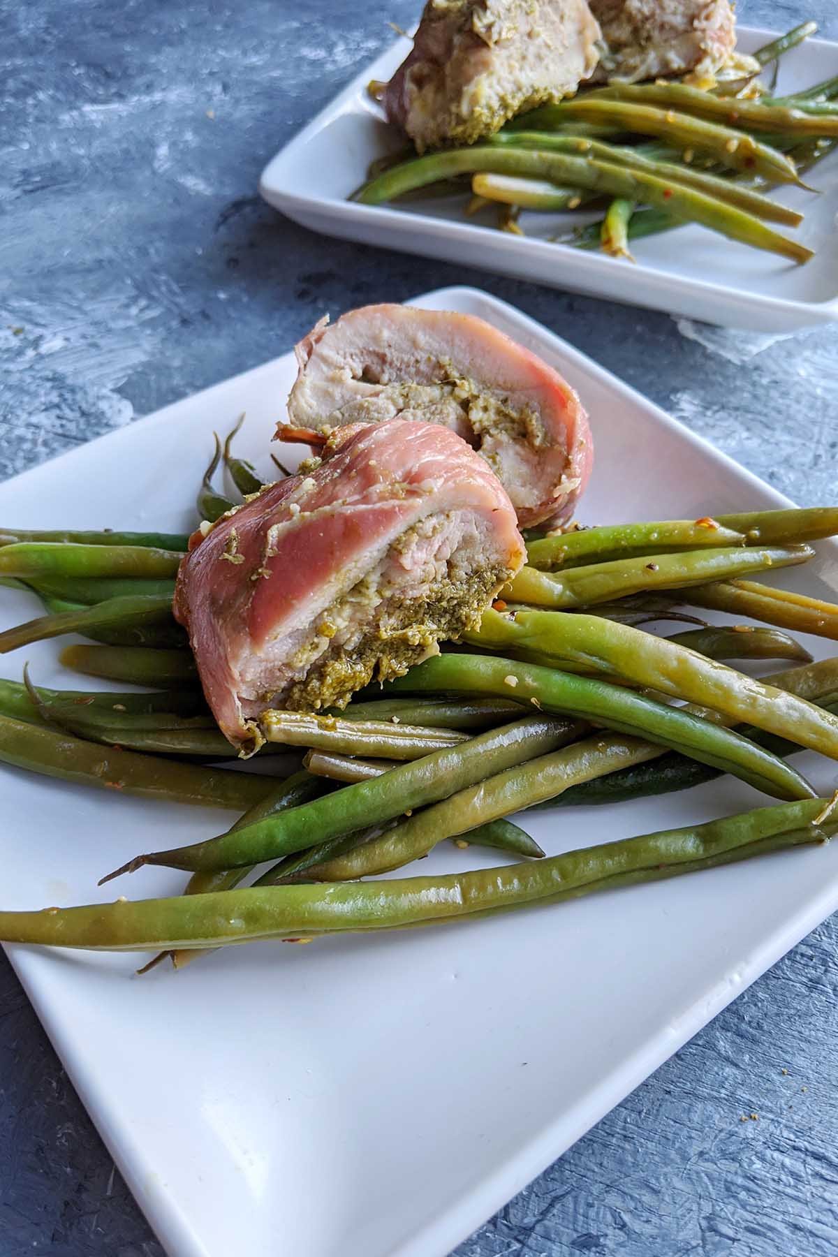 pesto stuffed chicken laying on a bed of green beans.