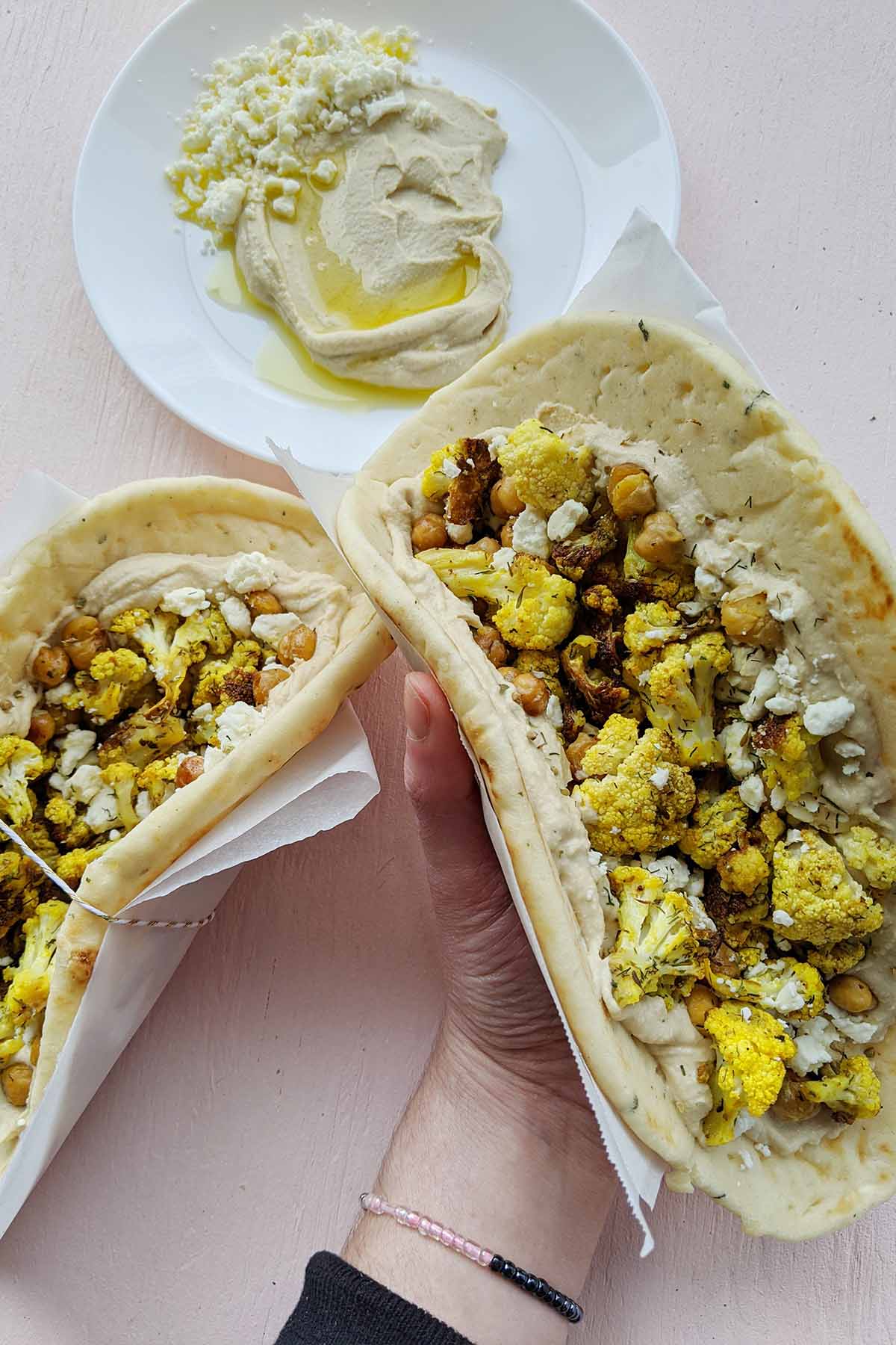 hand holding a wrap filled with hummus and roasted vegetables.