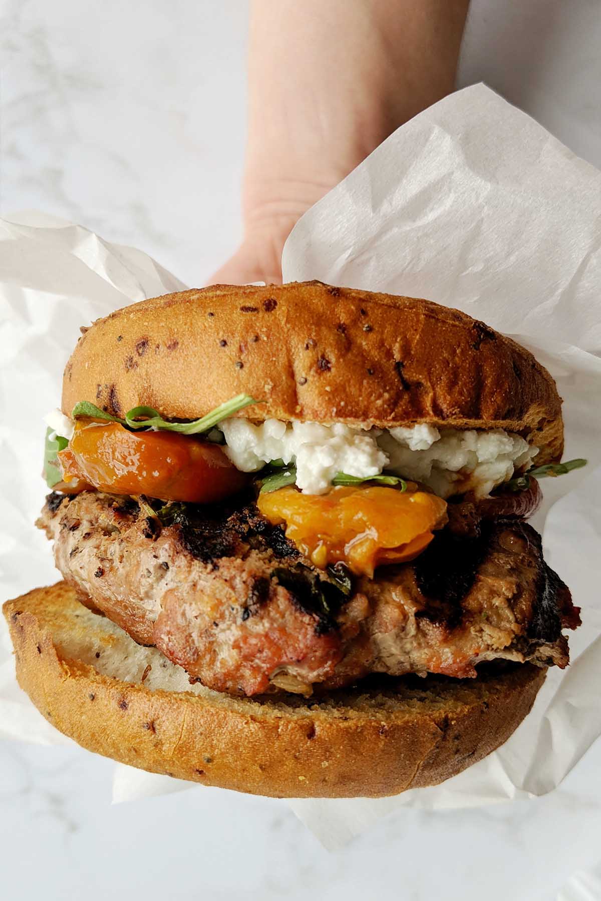 hand holding a turkey burger wrapped in parchment paper.