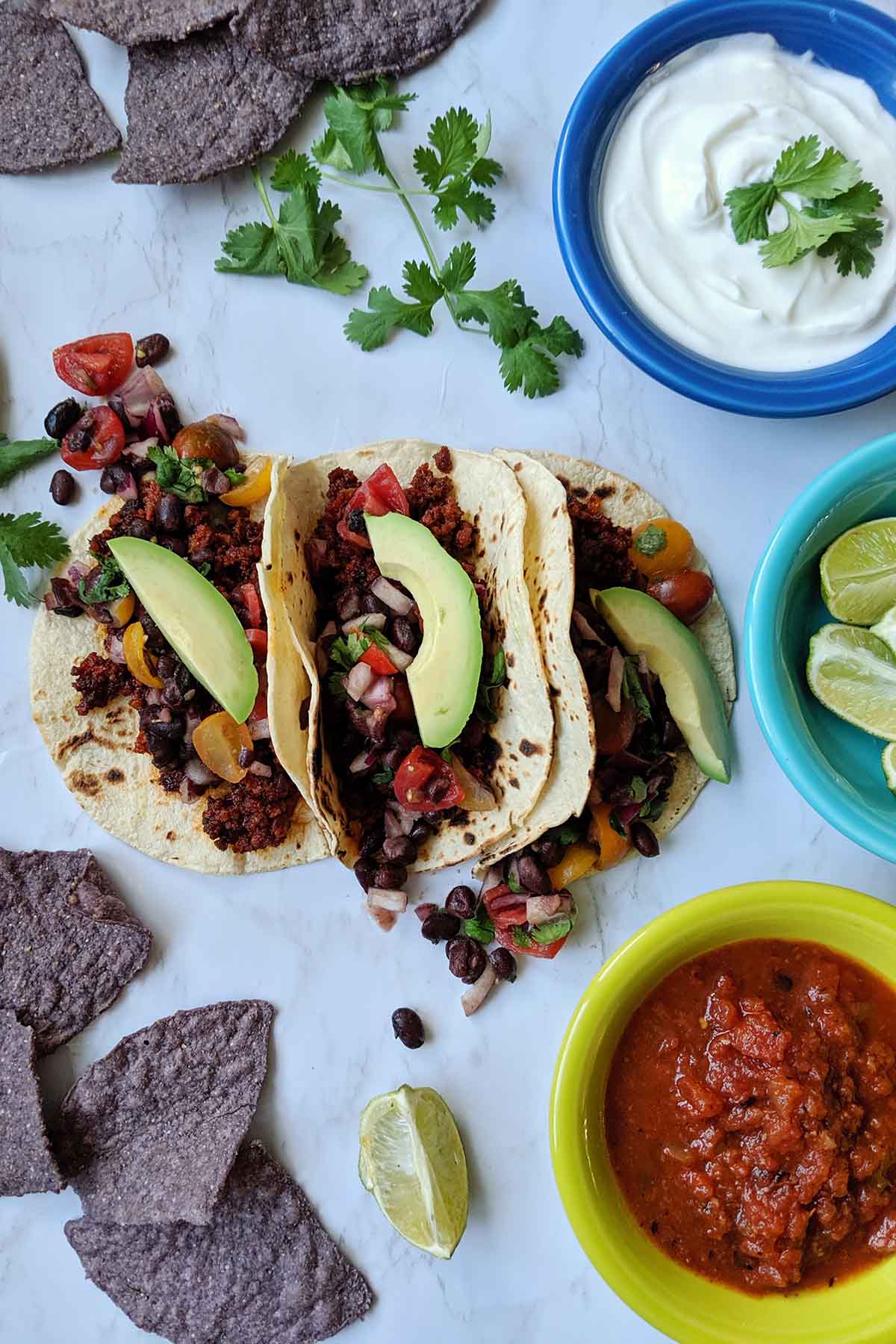 three chorizo tacos surrounded by tortilla chips and taco toppings.