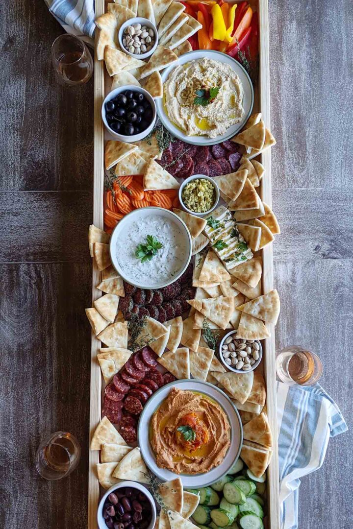 long Greek appetizer platter next to wine glasses.