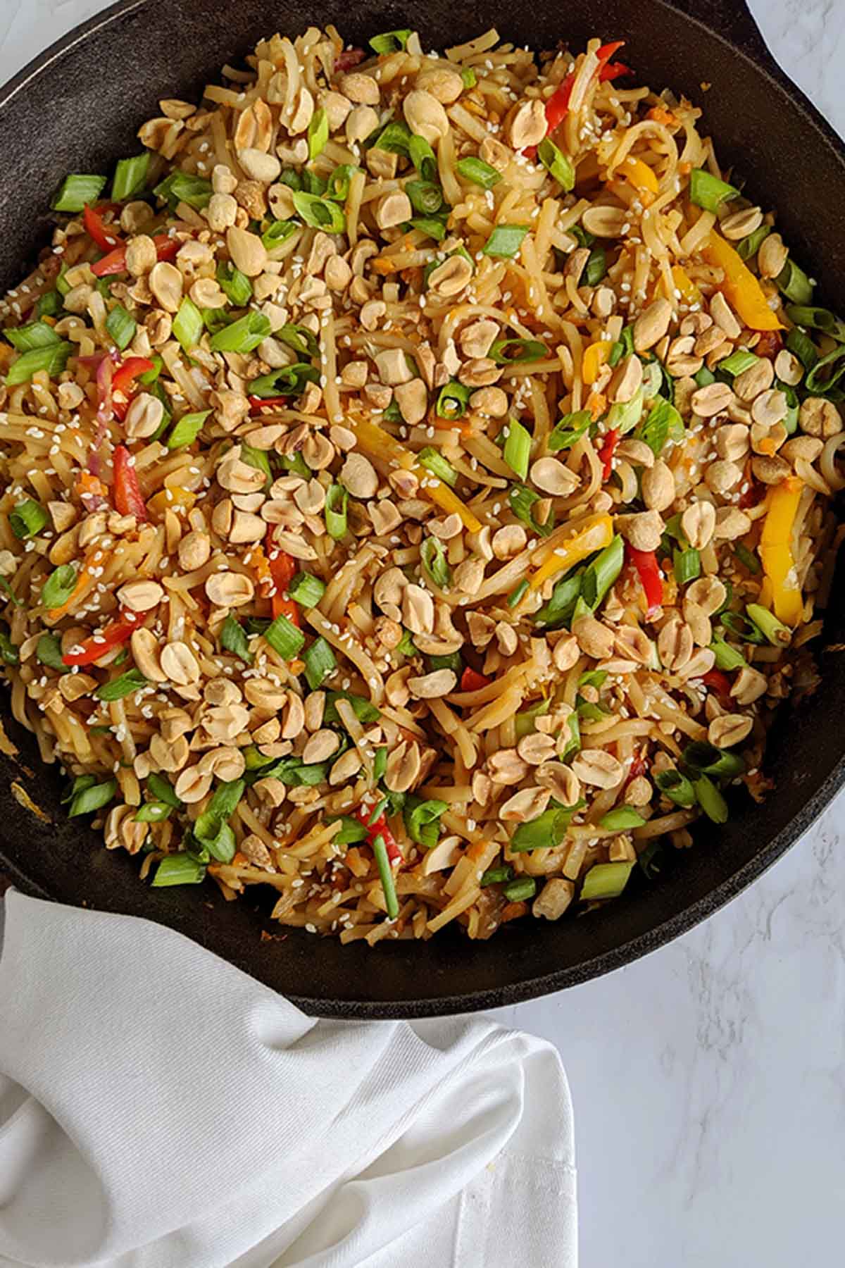 rice noodle stir fry topped with peanuts in a cast iron skillet.