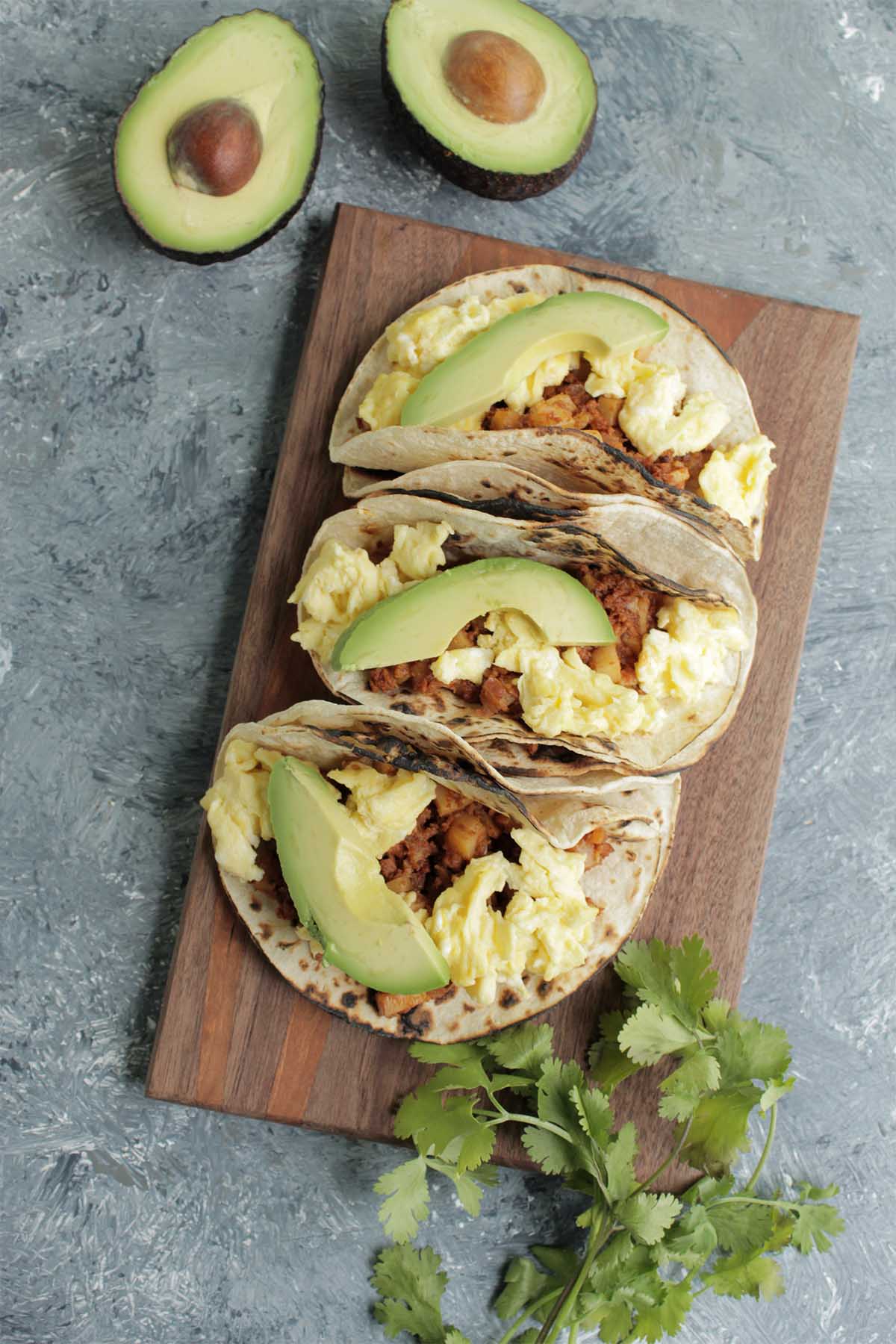 three chorizo and egg tacos on a wooden serving board.