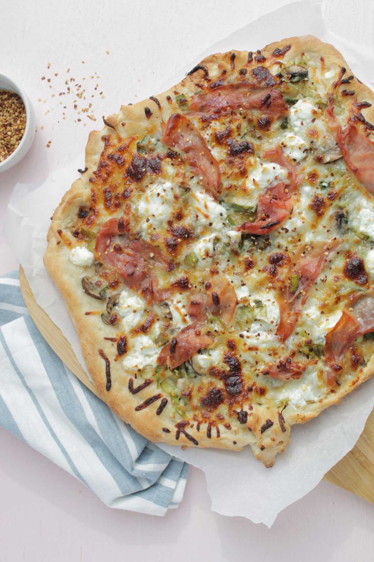 cooked pizza topped with mushroom, leek, and prosciutto.