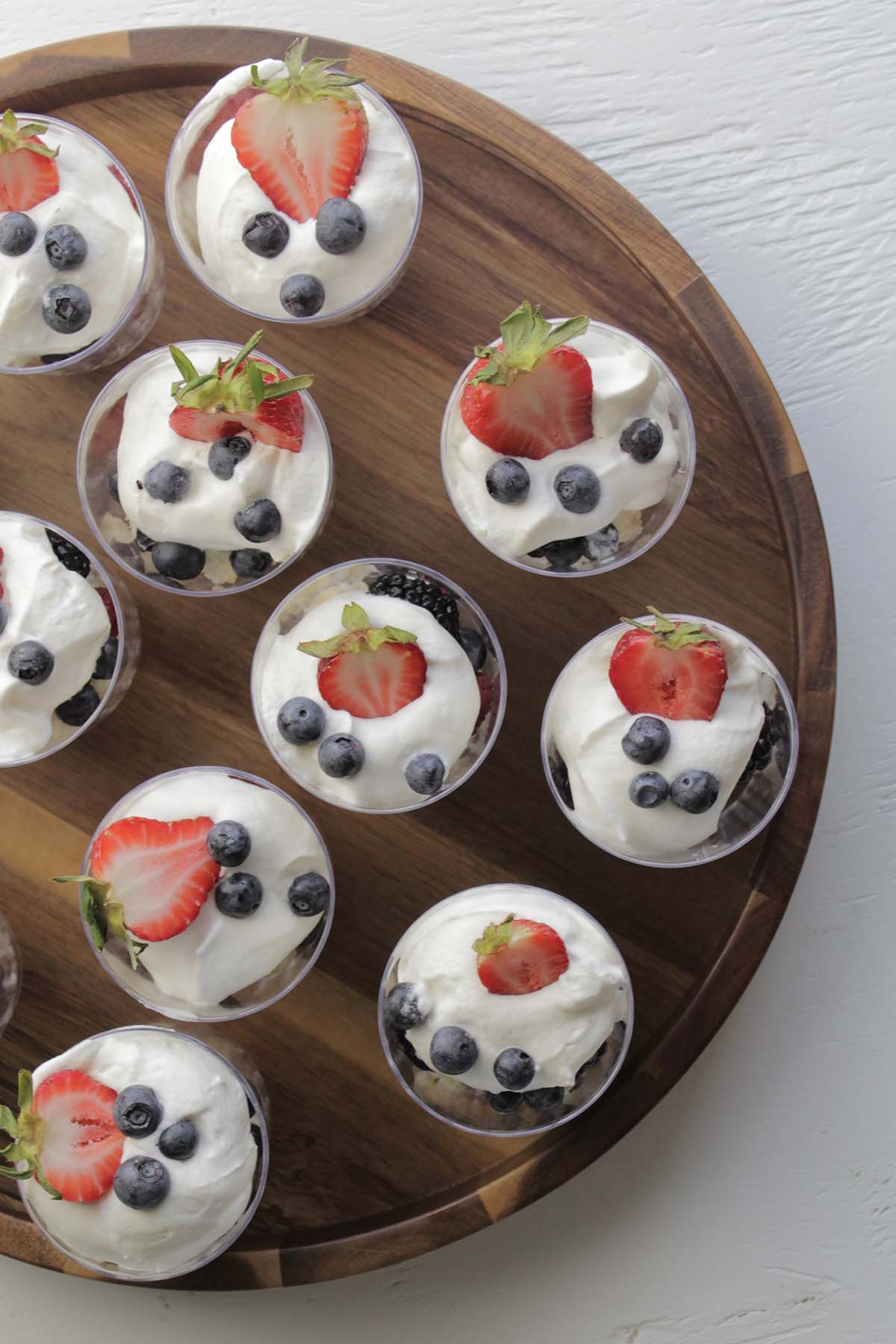 trifles with whipped cream and berries on a wooden tray.
