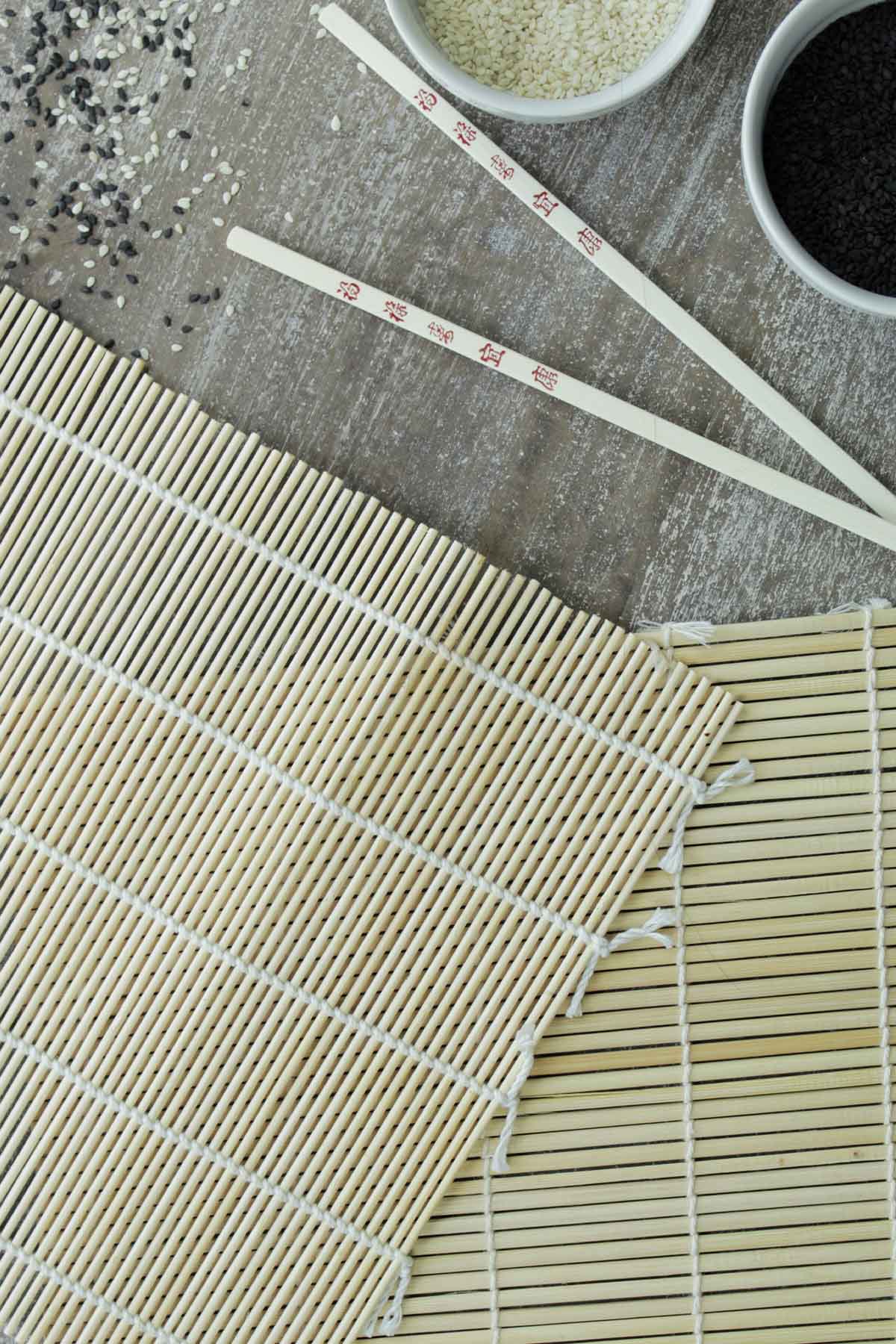 sushi rolling mat next to chopsticks and sesame seeds.