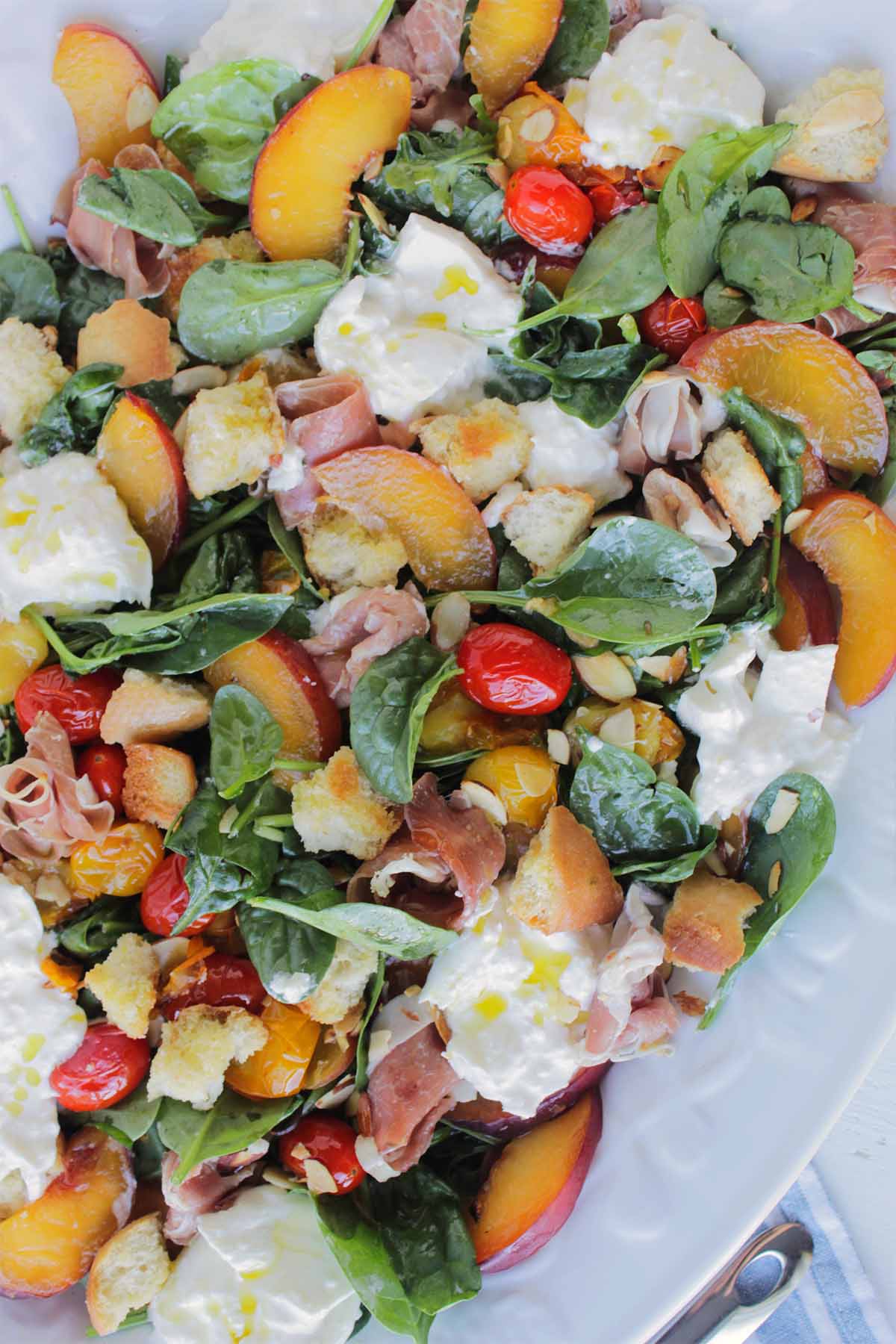 fresh salad filled with spinach, tomato, peach, and burrata.