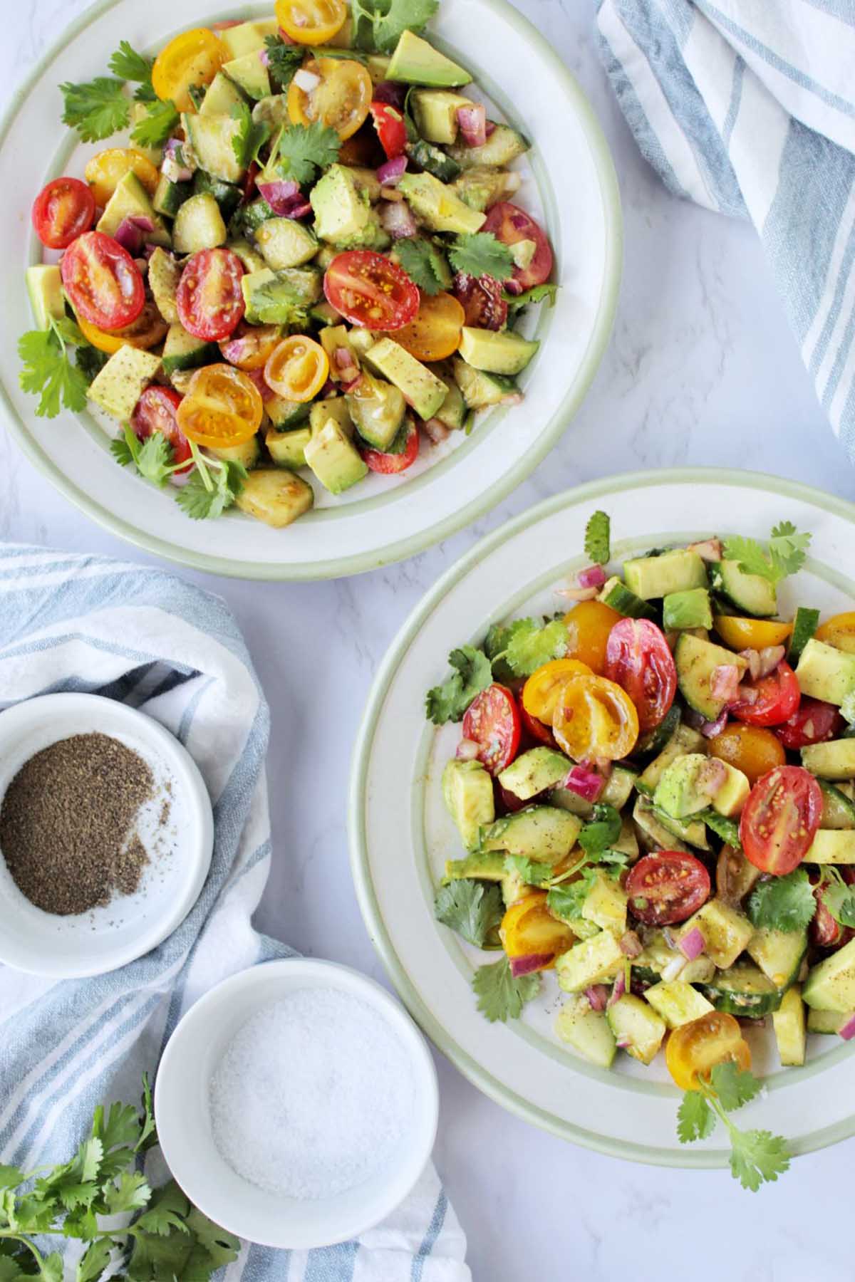 two plates filled with avocado salad next to small bowls of salt and pepper.