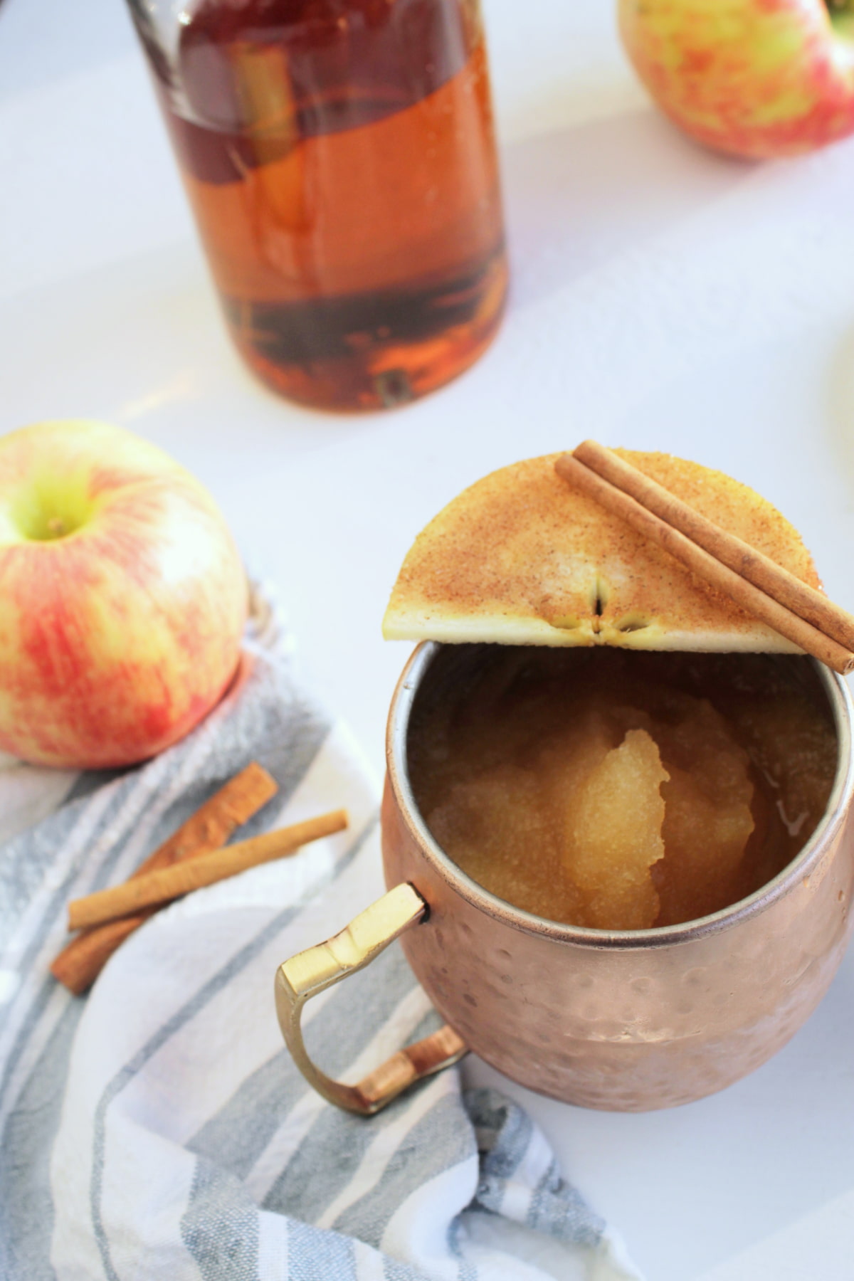 frozen alcoholic slushie in a copper mug garnished with apple slice.