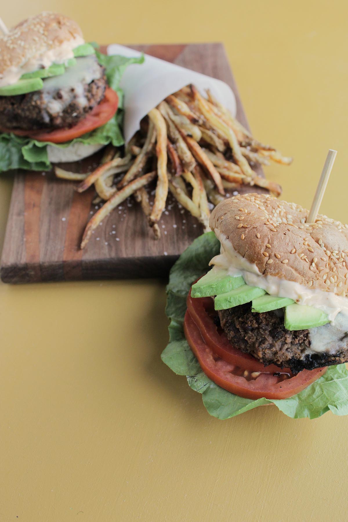 two black bean burgers loaded with toppings sitting next to french fries.