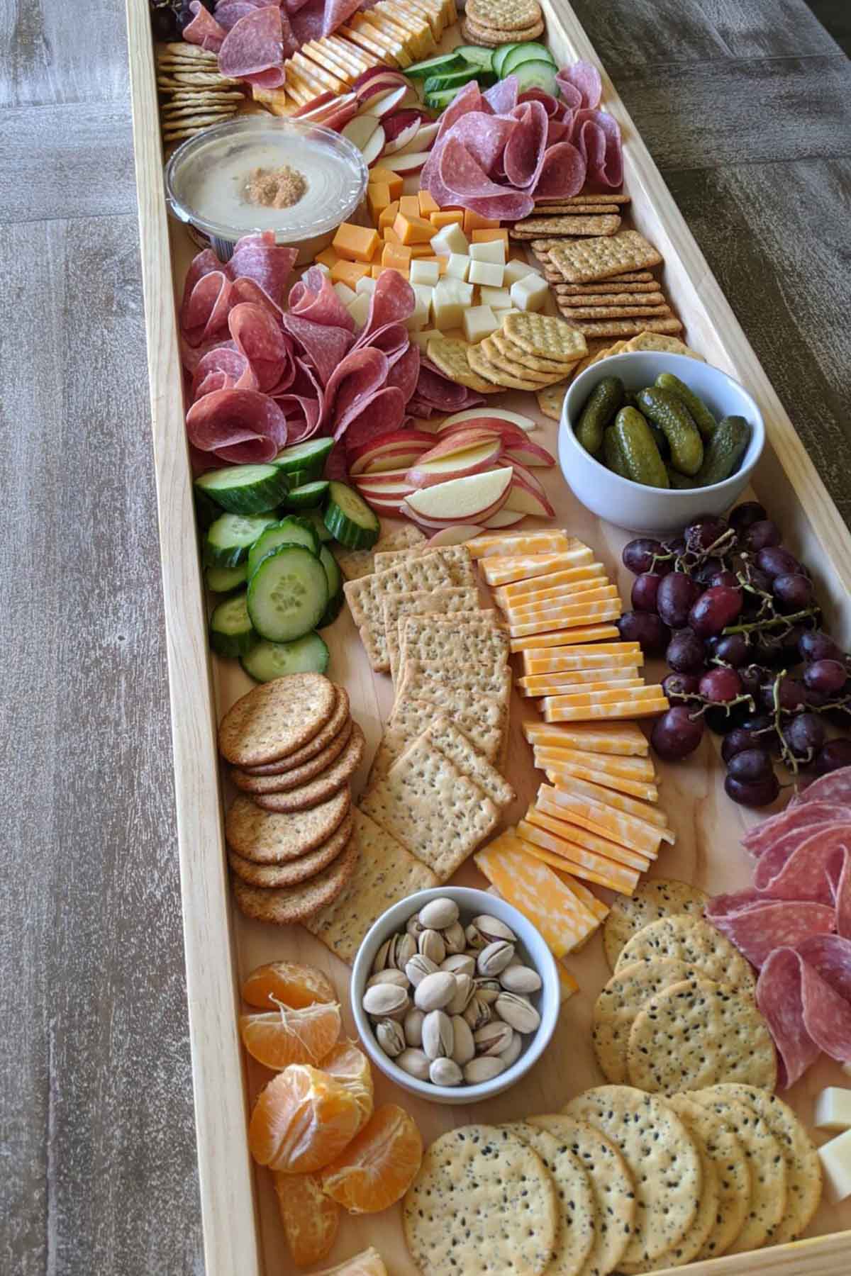 Long charcuterie board with meat, cheese, crackers, and various foods.