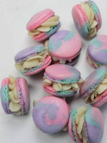 rainbow macarons in a pile on a white background.