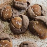 chocolate cookies filled with caramel laying on a surface sprinkled with cocoa powder.
