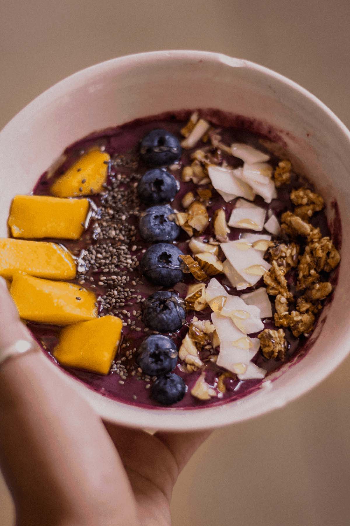 hand holding acai berry smoothie bowl with toppings.