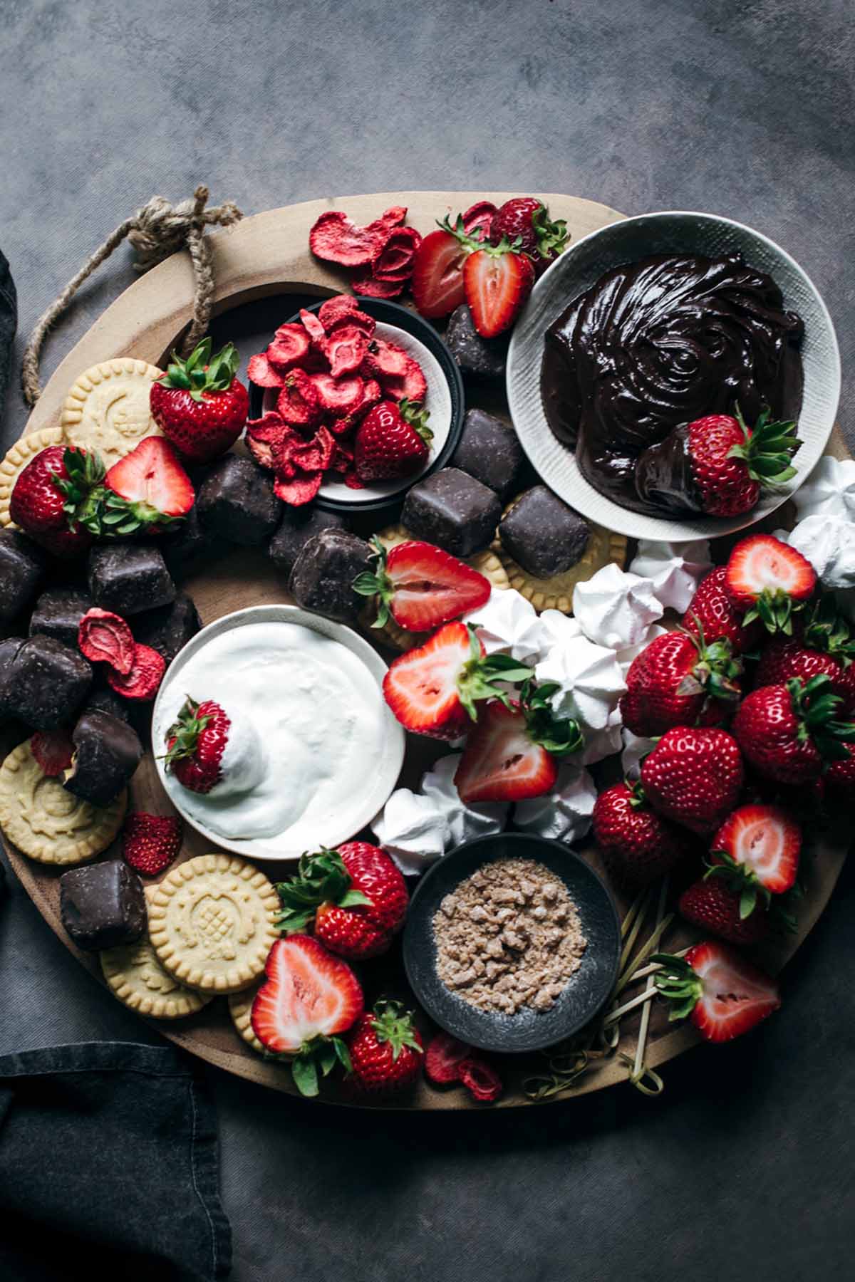 wooden cutting board layered with strawberries, chocolate, and cream.