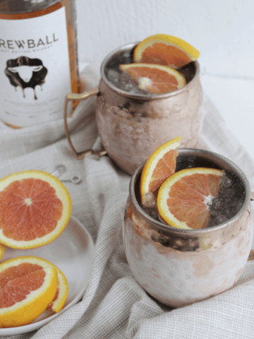 Skrewball whiskey drinks in copper mugs garnished with grapefruit slices.