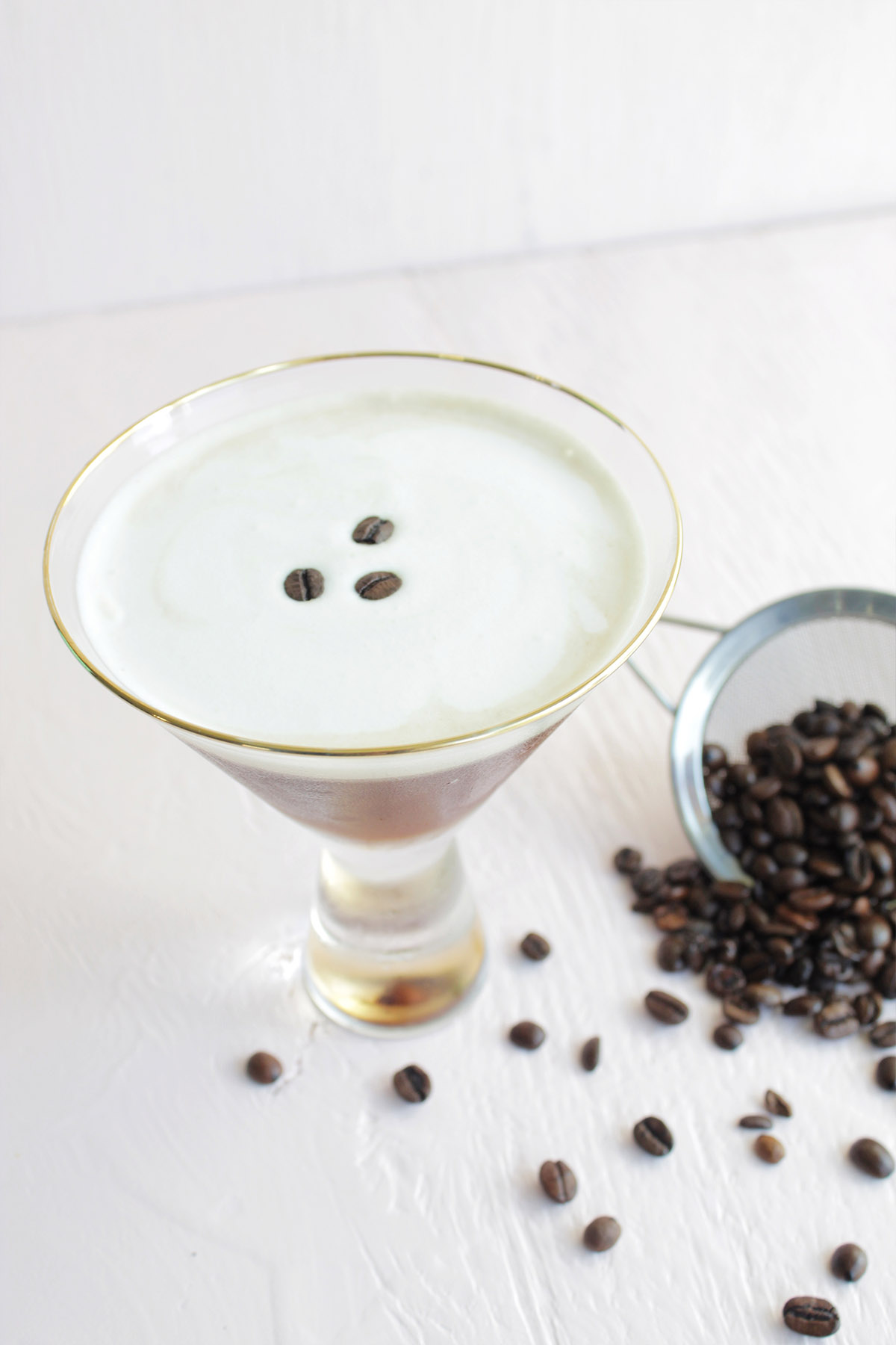 espresso martini with white foam and three coffee beans on top.