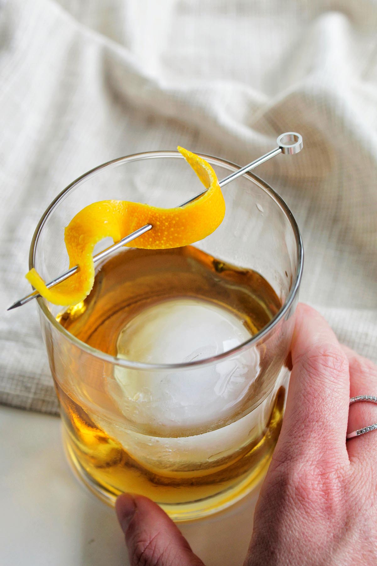 old fashioned cocktail with large ice and orange twist.
