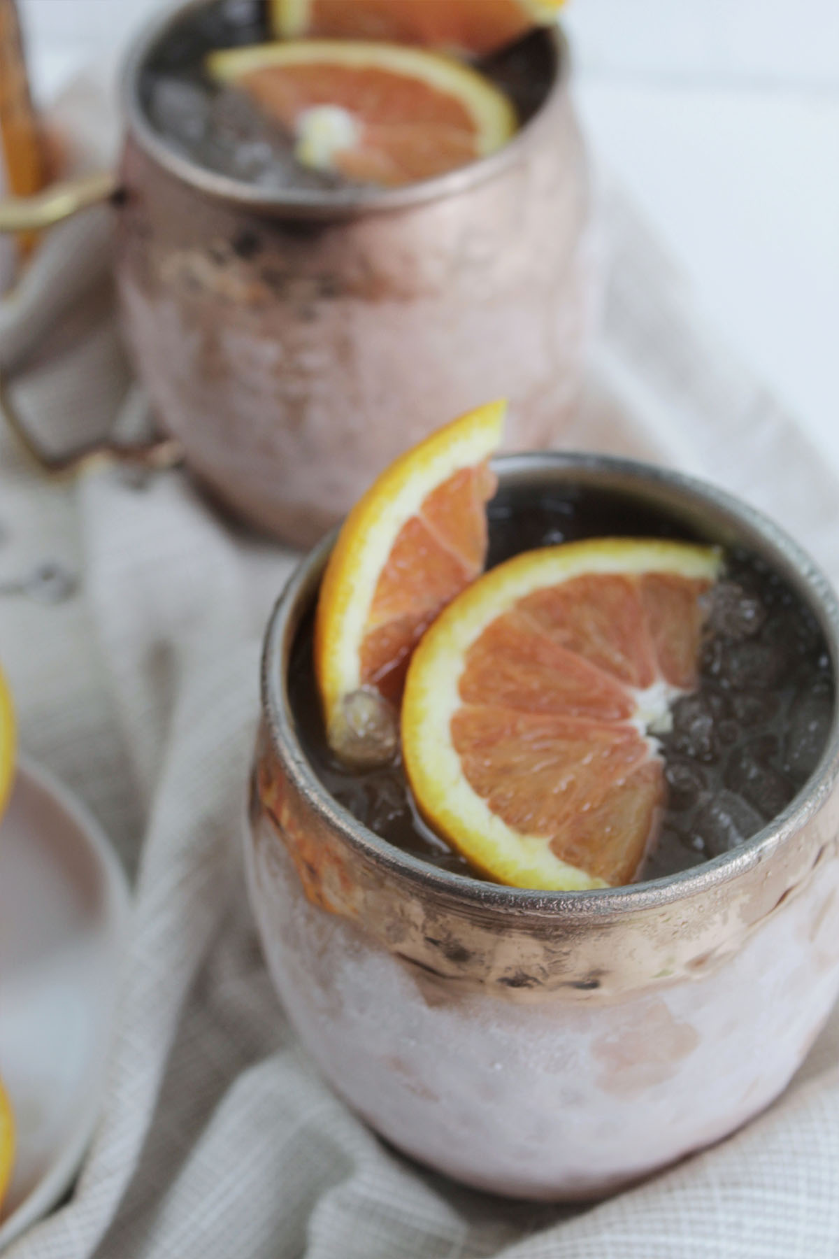 two moscow mule cocktails in chilled copper mug with orange slices.