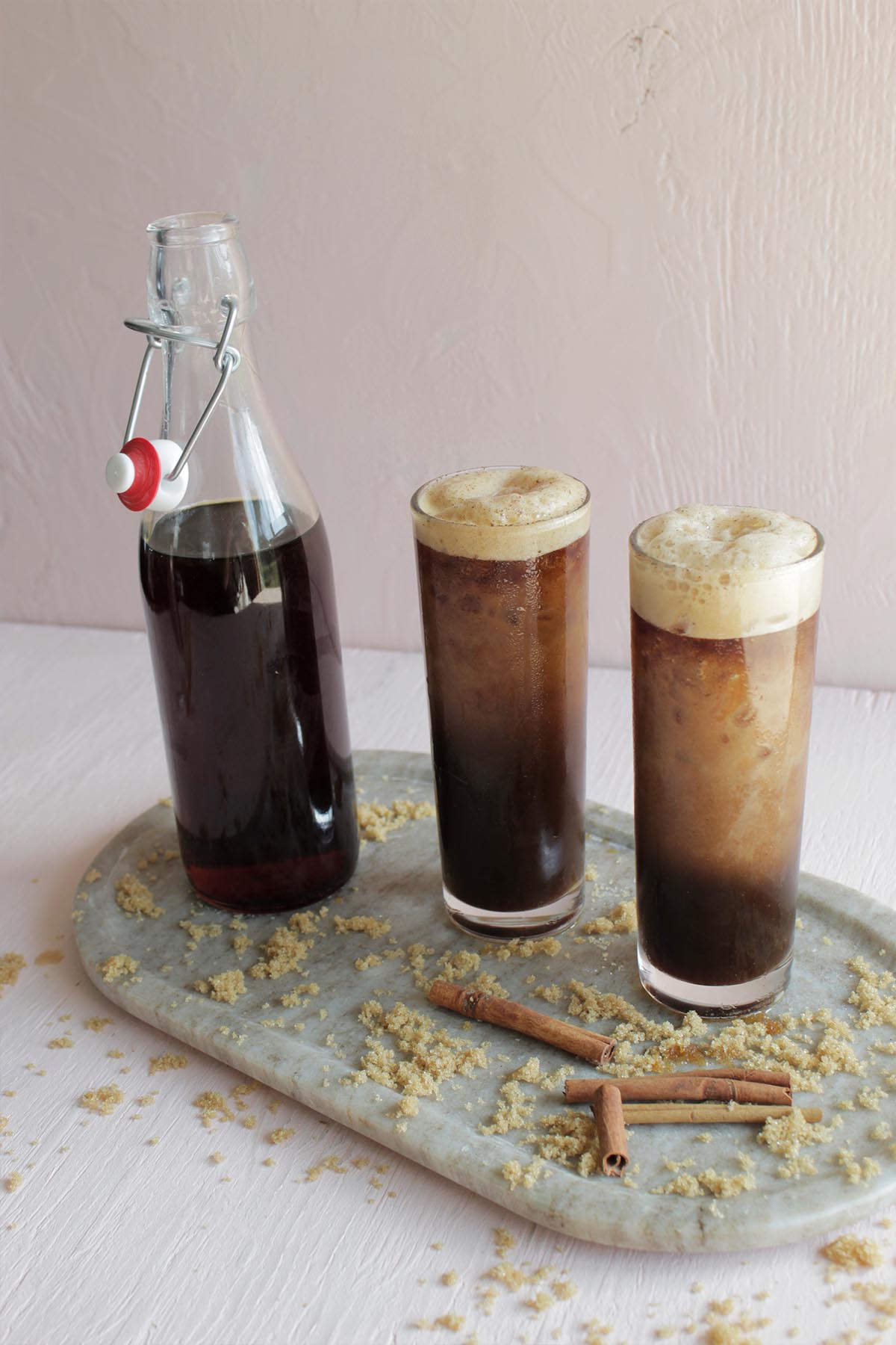 two highball glasses with cold brew next to glass bottle filled with brown syrup.