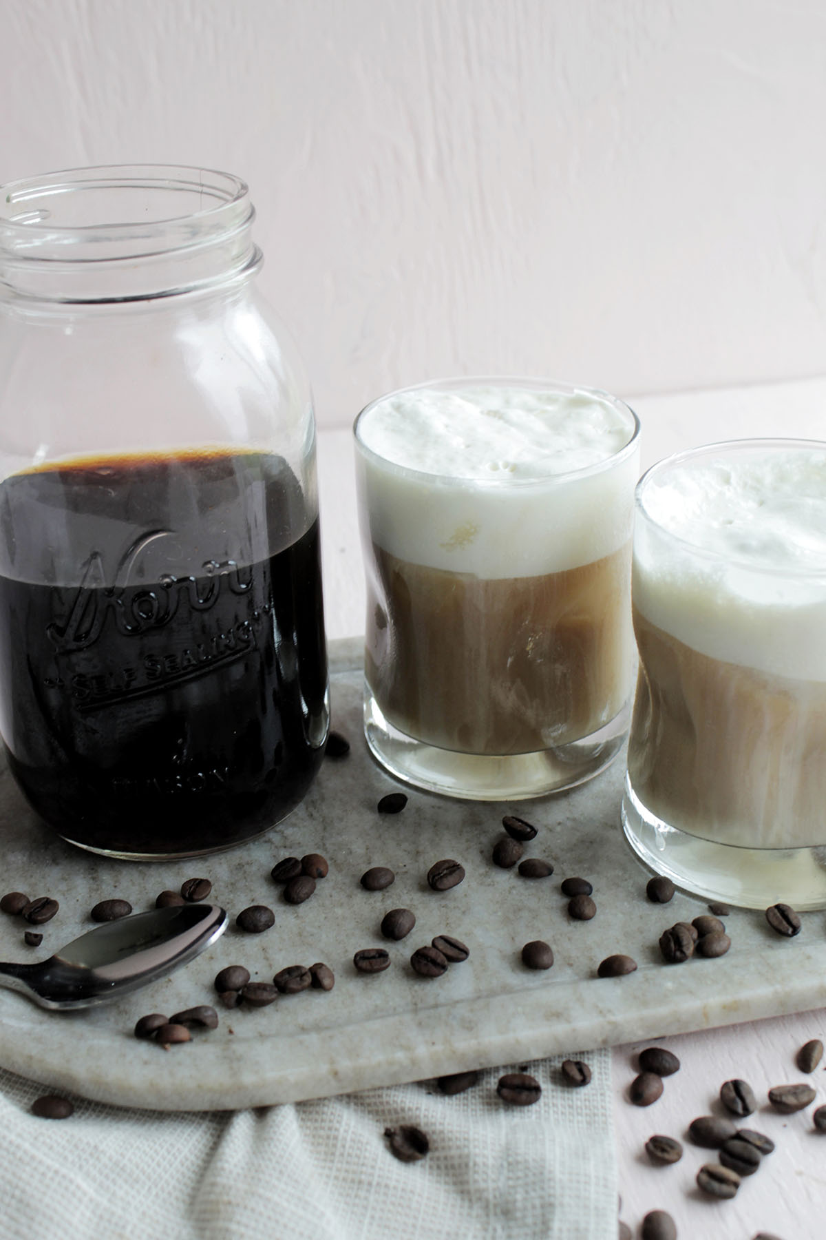 cold brew coffee in mason jar next to two glasses of coffee with cold foam.