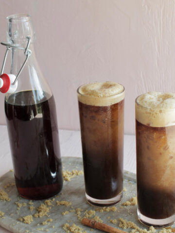 two highball glasses with cold brew next to glass bottle filled with brown syrup.