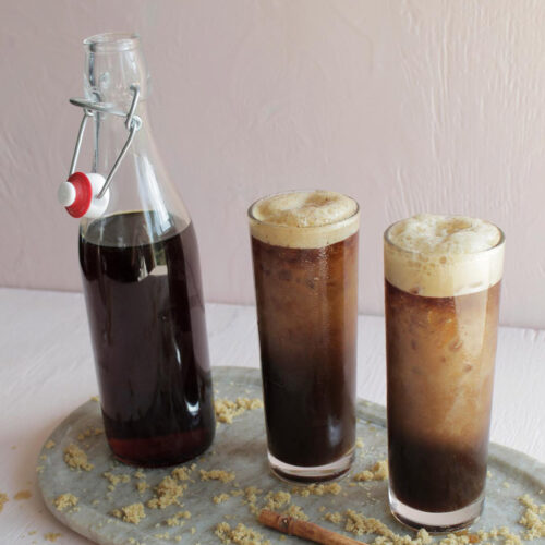 two highball glasses with cold brew next to glass bottle filled with brown syrup.
