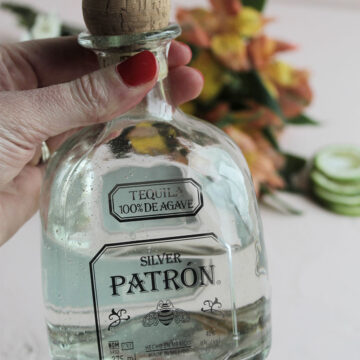 Silver Patron Tequila bottle in front of flowers.