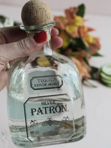 girl with red fingernails holding a bottle of Silver Patron.