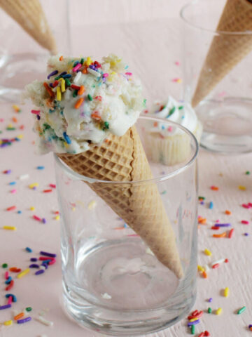 birthday cake ice cream scoop in waffle cone topped with rainbow sprinkles.