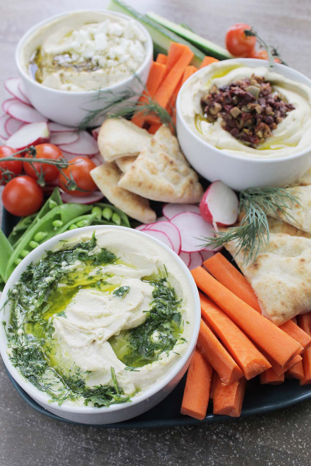 three types of hummus on a platter with vegetables and pita.