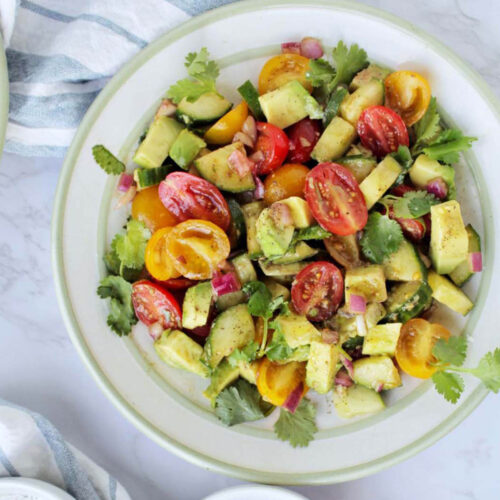 plate of salad with cherry tomatoes, cucumbers, cilantro and avocado.