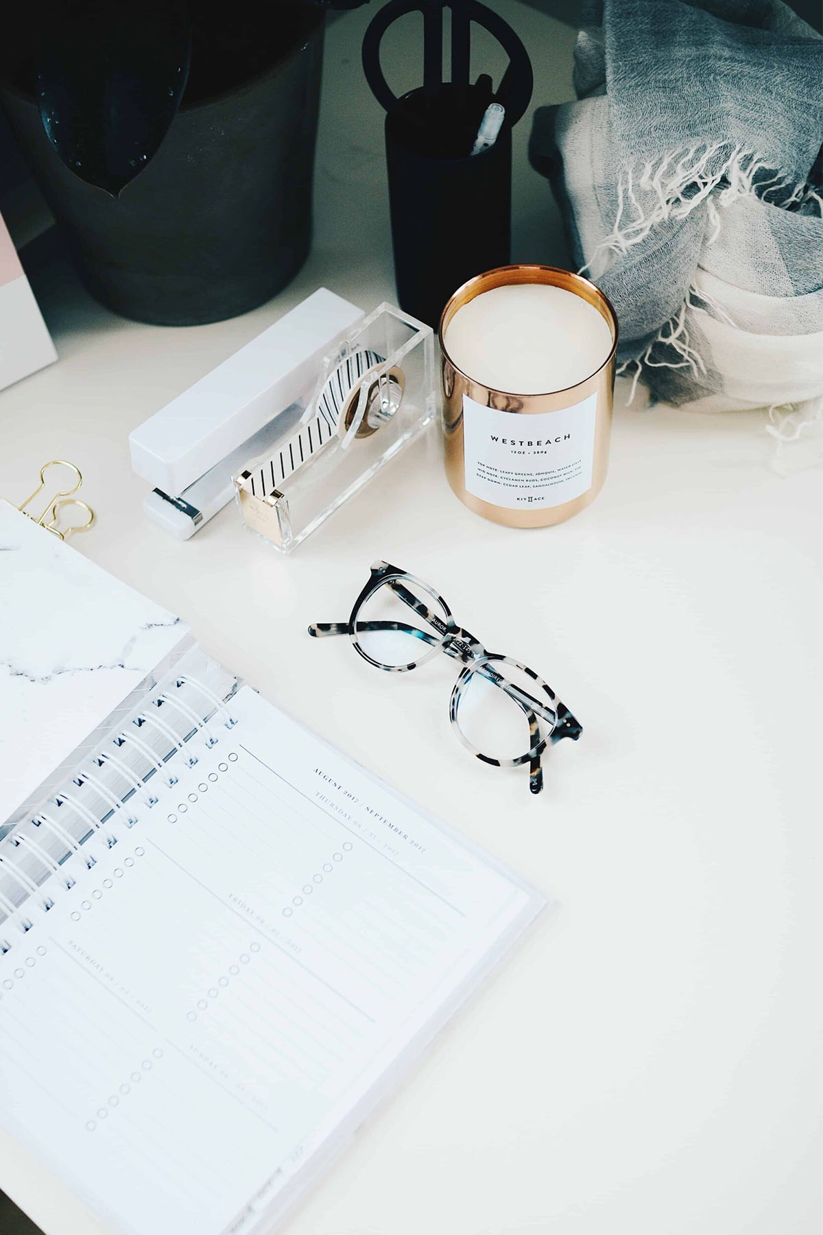 desk with planner, glasses, and candle on top
