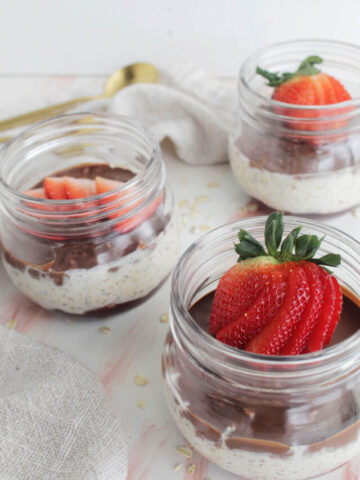 fanned strawberries topping chocolate overnight oats in glass jars.