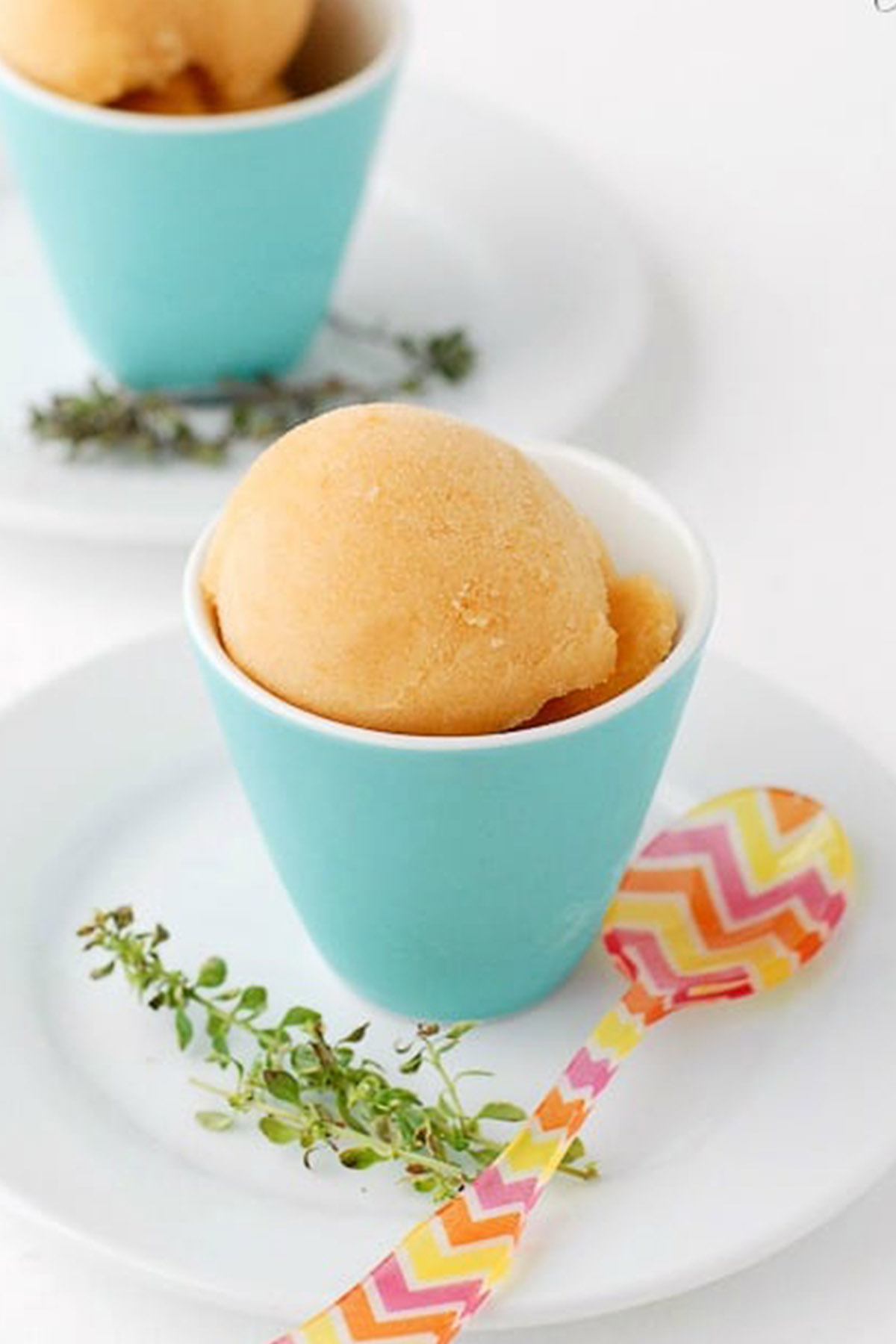 peach sorbet in blue serving bowl next to a spoon.