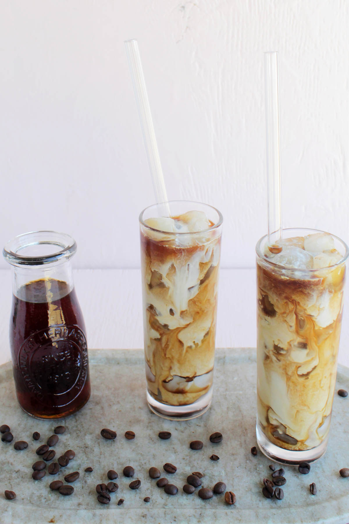 two cups filled with cold brew surrounded by coffee beans.