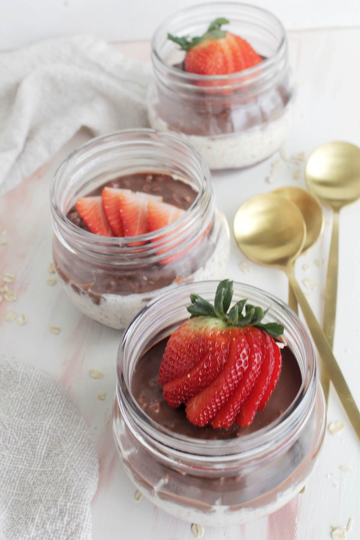 strawberry overnight oats in mason jars next to gold spoons.
