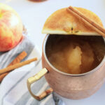 apple cider bourbon slushie in copper mug with apple slice on top.