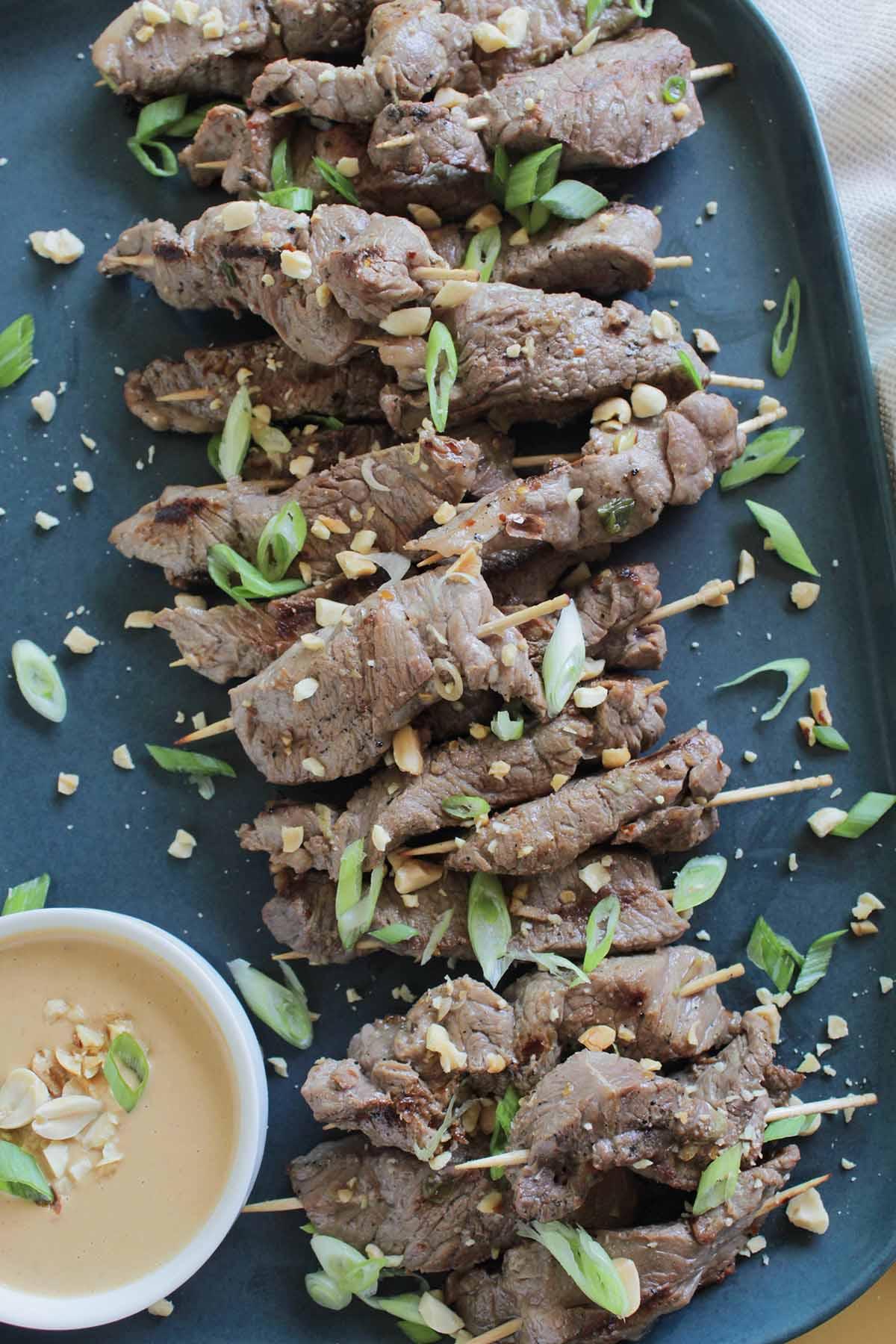 Asian beef skewers next to dipping sauce.