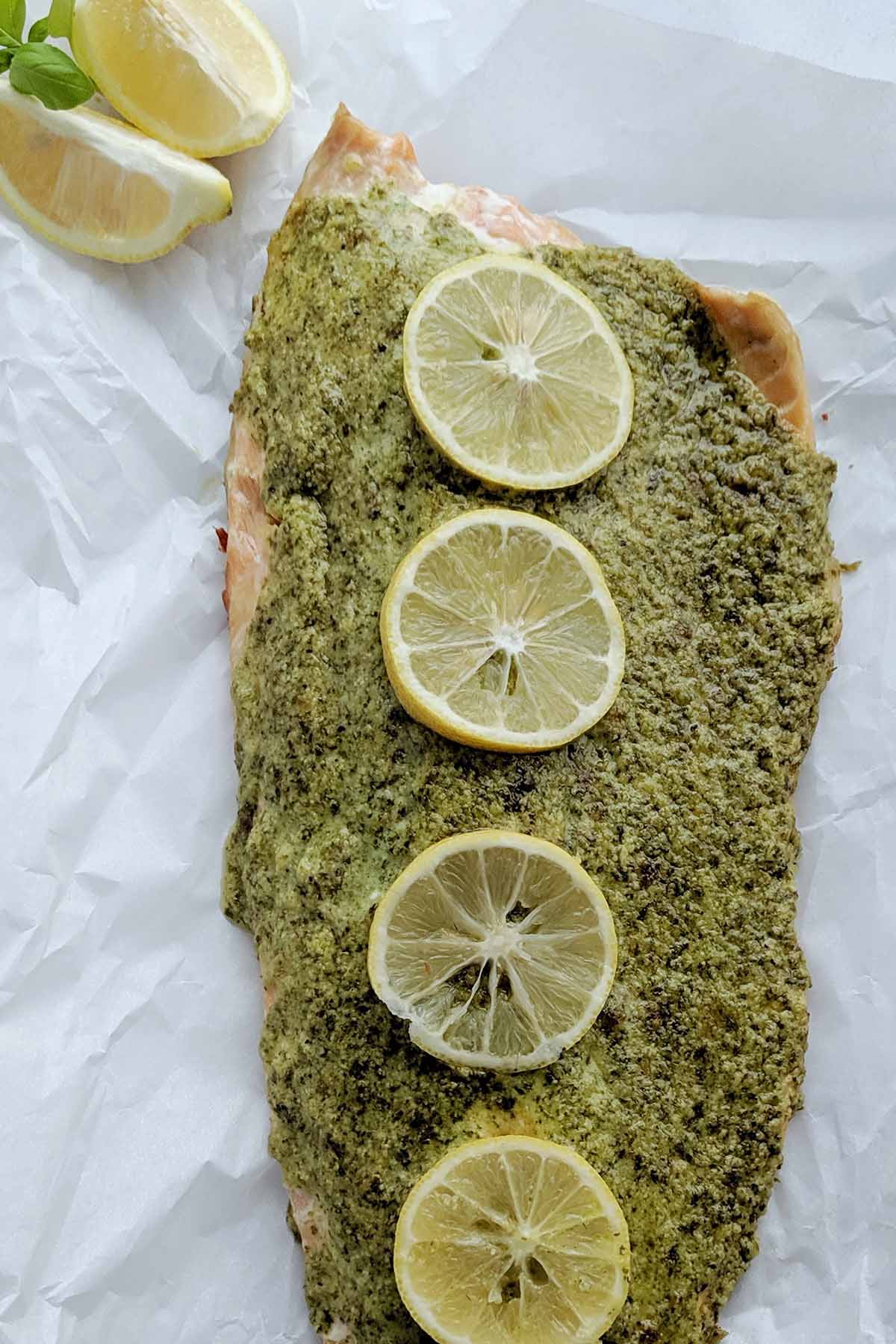 cooked salmon filet with green herb sauce topped with lemon slices.