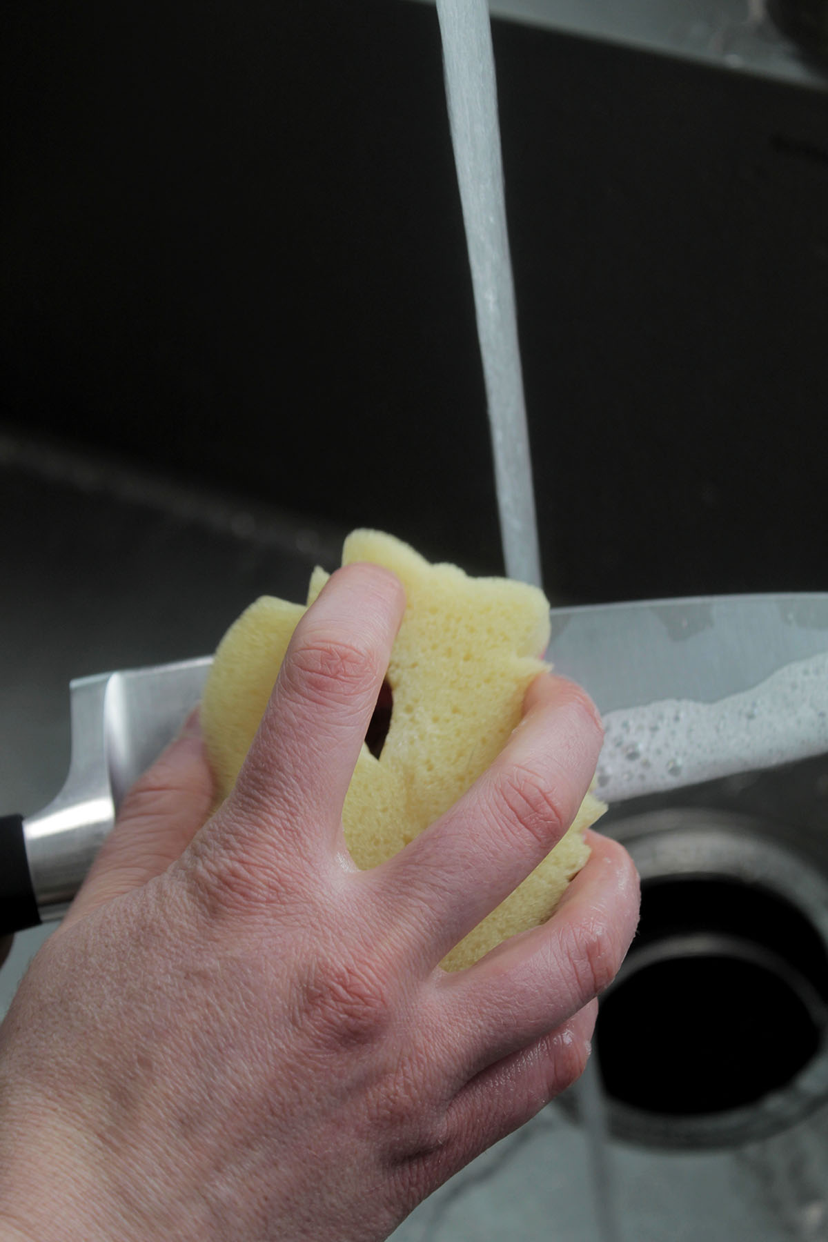 washing a chef's knife with a sponge.