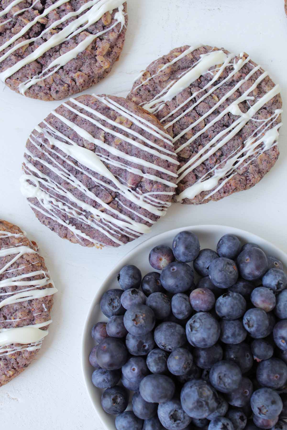 blueberry cookies with white chocolate drizzle next to bowl of blueberries.
