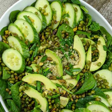 spinach salad with green toppings in a large white serving bowl.