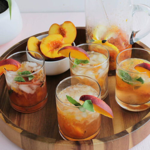 four low ball cocktail glasses filled with a peach cocktail resting on wooden serving tray.