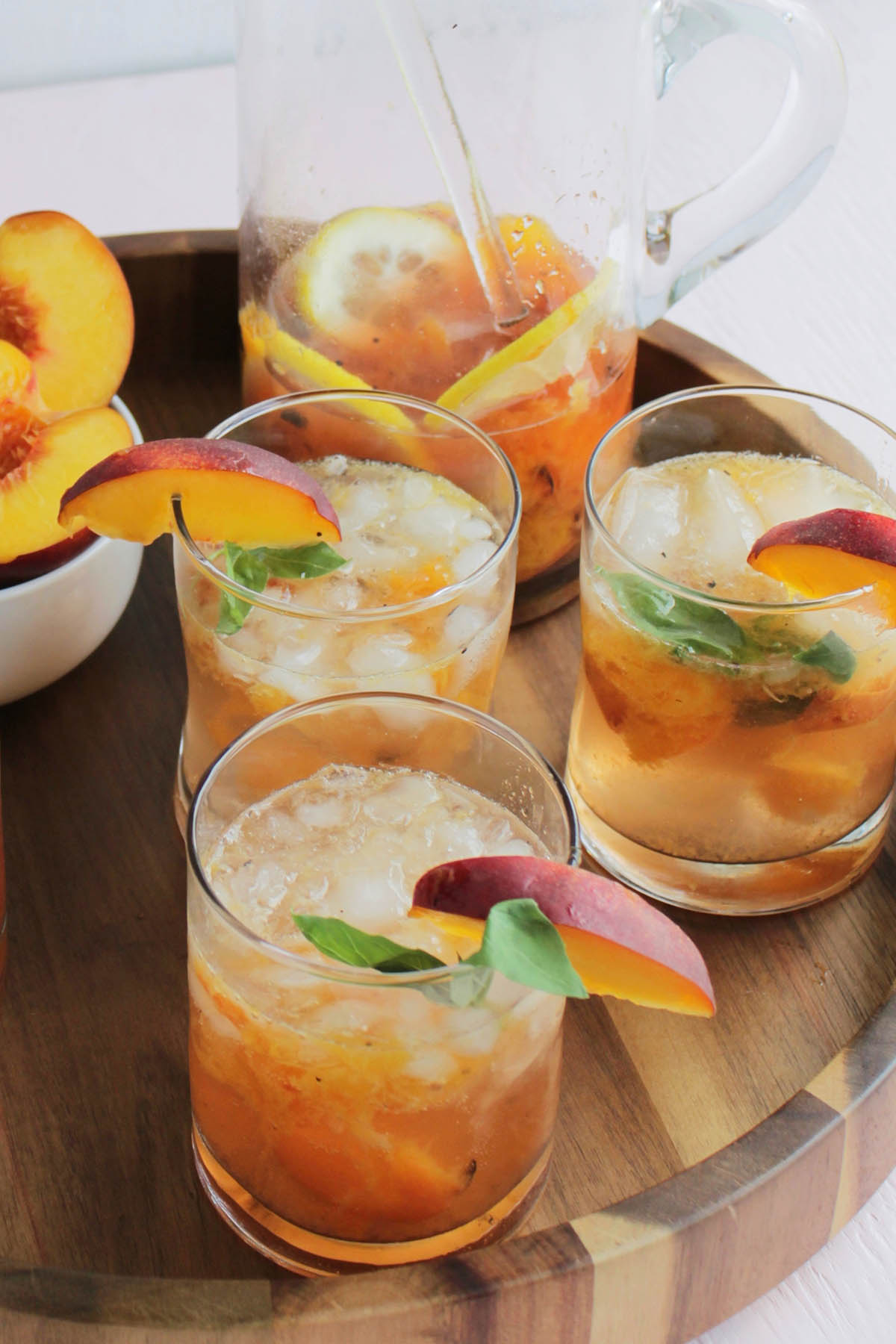 three low ball glasses full of an orange cocktail mixture next to a glass pitcher.