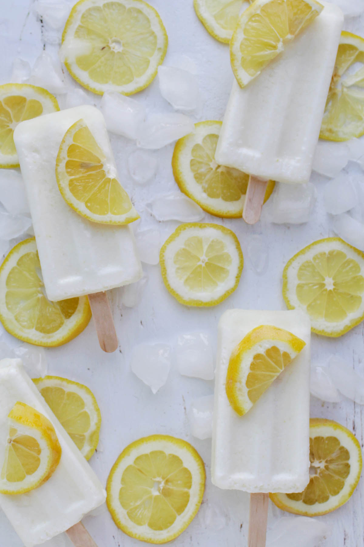 four lemon popsicles laying on ice and lemon slices.