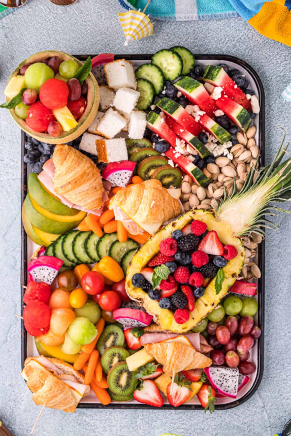 platter filled with summer fruit, vegetables, and croissant sandwiches.