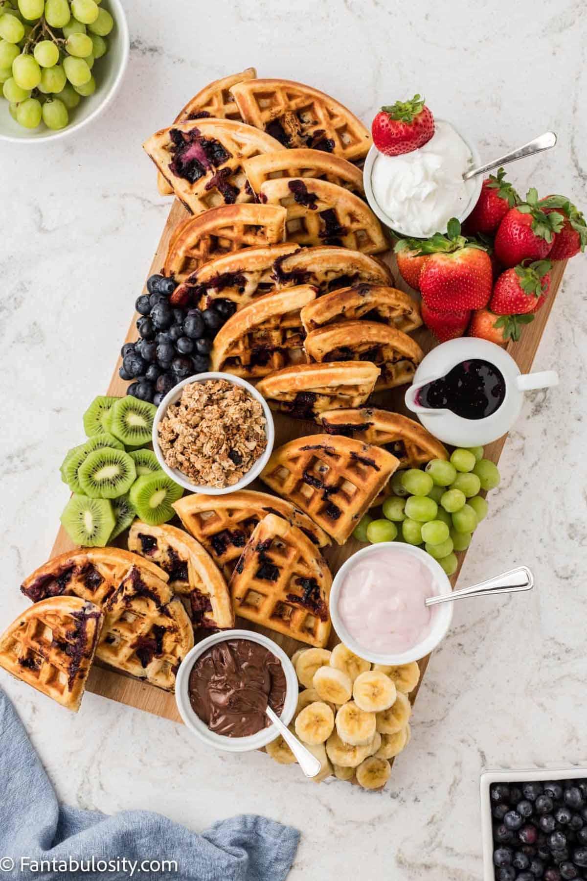 waffles with fruit and dip on a wooden cutting board.