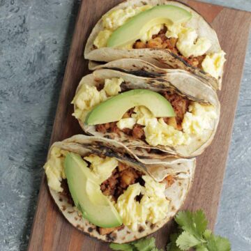 three chorizo tacos topped with an avocado slice laying on wooden cutting board.