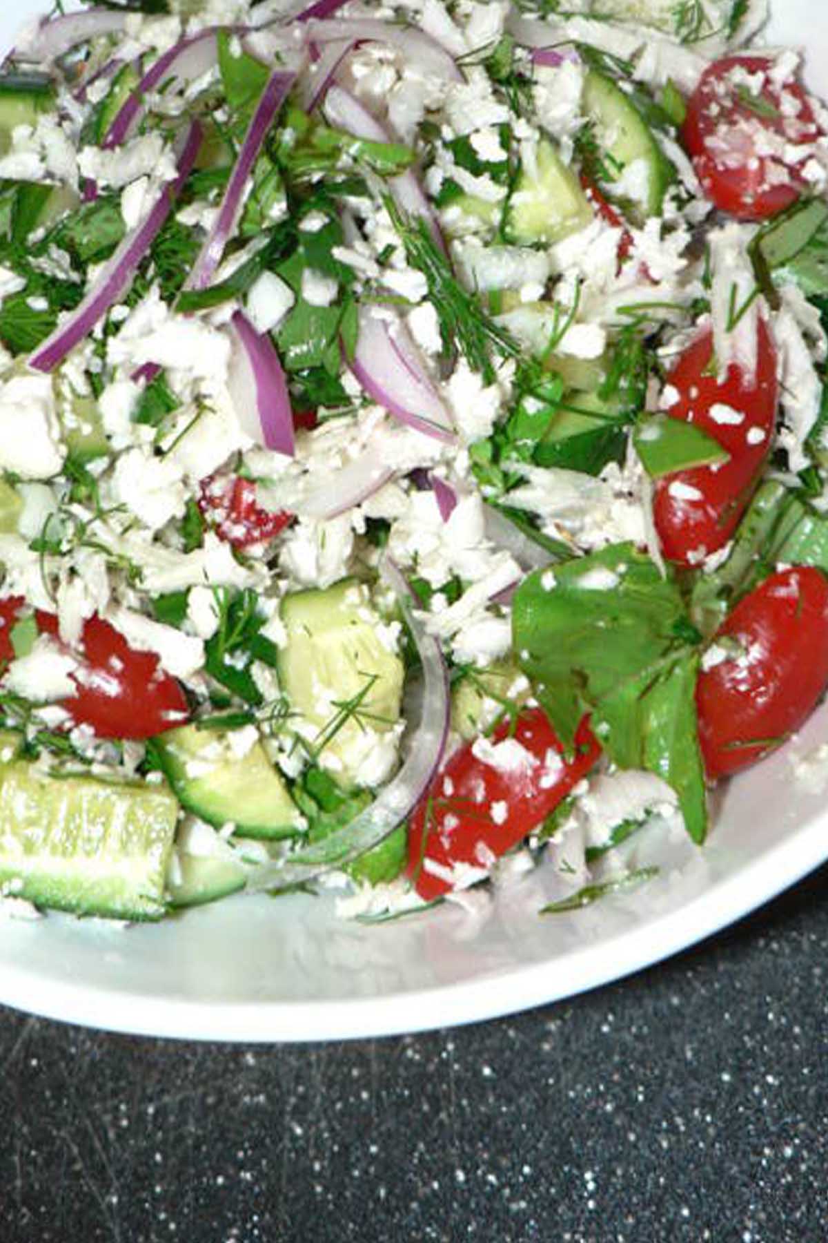 salad with cucumber, red onions, and tomato in a white bowl.